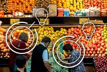 Shoppers selecting fresh fruits and vegetables at a colorful grocery store produce section with apples, oranges, and other fruits neatly arranged on shelves.