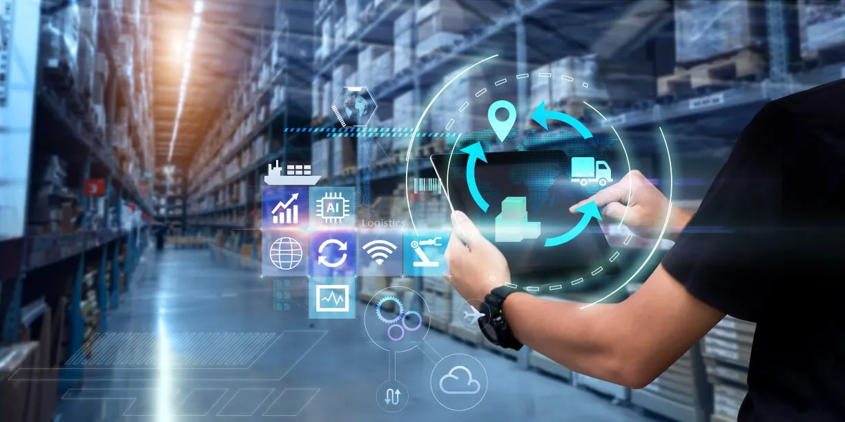 Person holding a tablet with digital supply chain and logistics icons overlaid, set against the blurred background of a large warehouse filled with shelves and boxes.