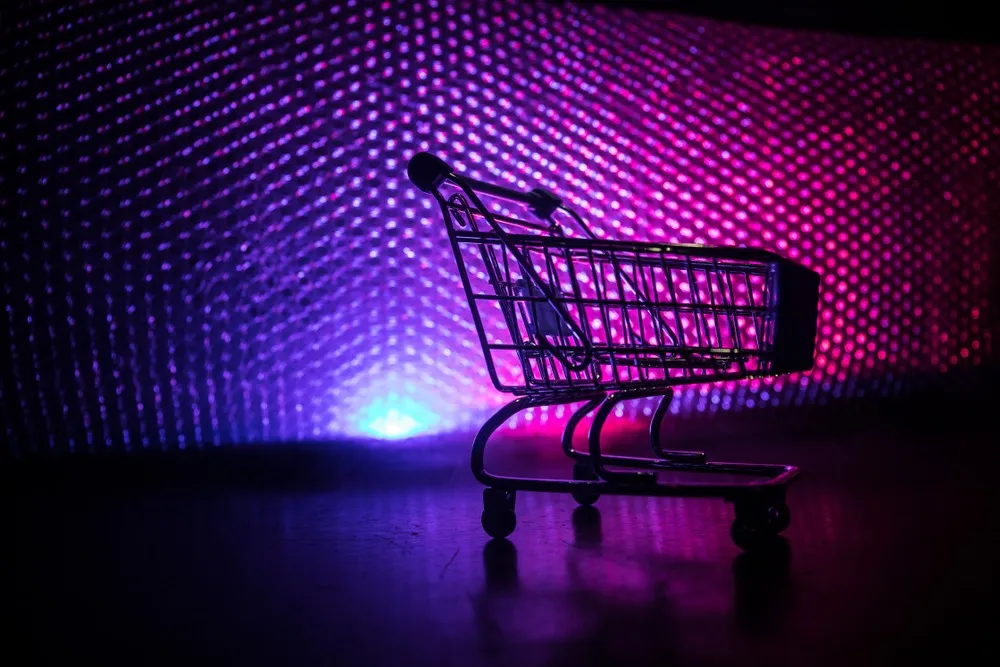 Empty miniature shopping cart silhouette against a vibrant purple and pink illuminated dotted background.