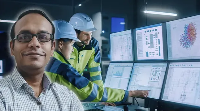 Three professionals in a control room with six monitors displaying technical data and graphs; two are wearing safety helmets and high-visibility jackets, one is smiling at the camera.