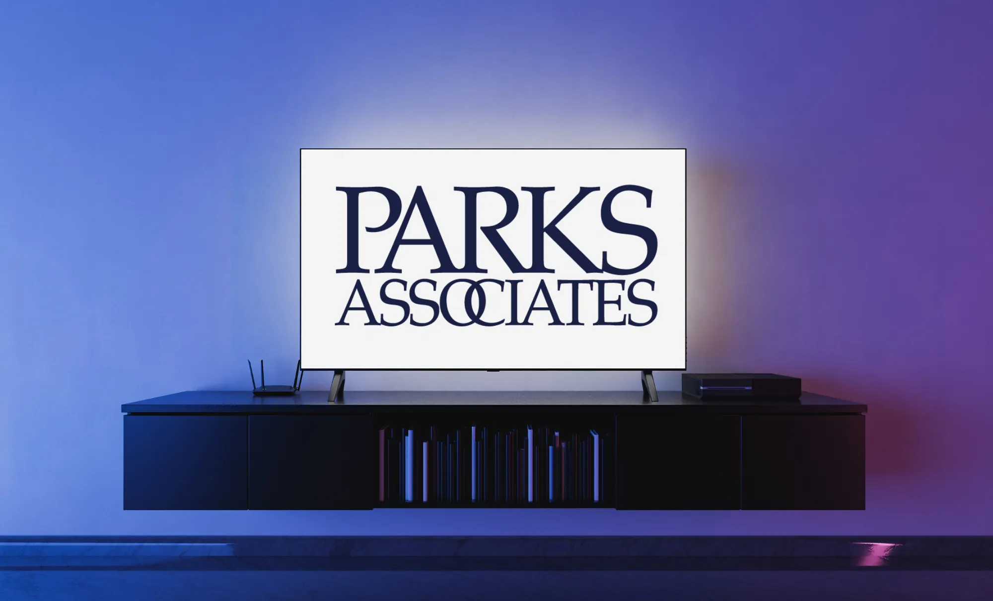 Modern living room with a wall-mounted flat-screen TV displaying the text 'PARKS ASSOCIATES' in bold navy font, with overlapping O's in Associates, above a sleek black media console with books and electronic devices.