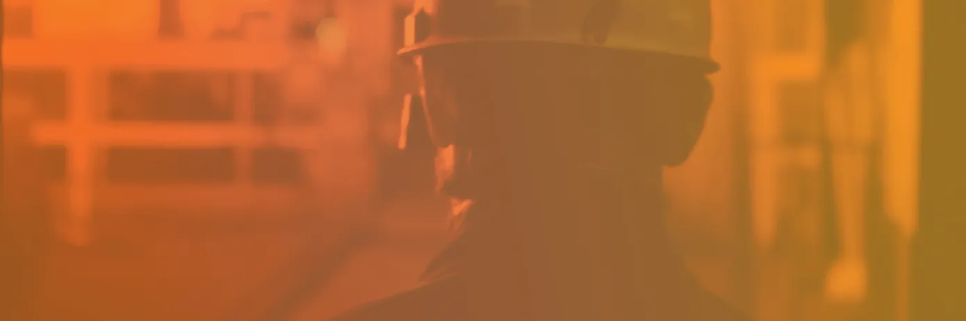 Silhouette of a person wearing a hard hat and safety glasses in an industrial setting with orange lighting.