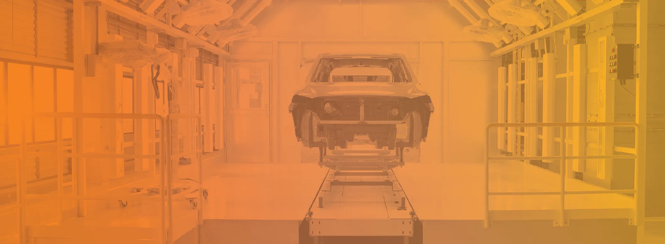 An unfinished car body frame positioned on a conveyor inside an industrial automotive manufacturing or assembly plant.