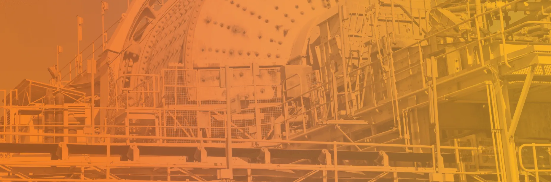 Large industrial machinery with metal framework, platforms, pipes, and a cylindrical drum-like structure with bolts, covered by an orange filter.
