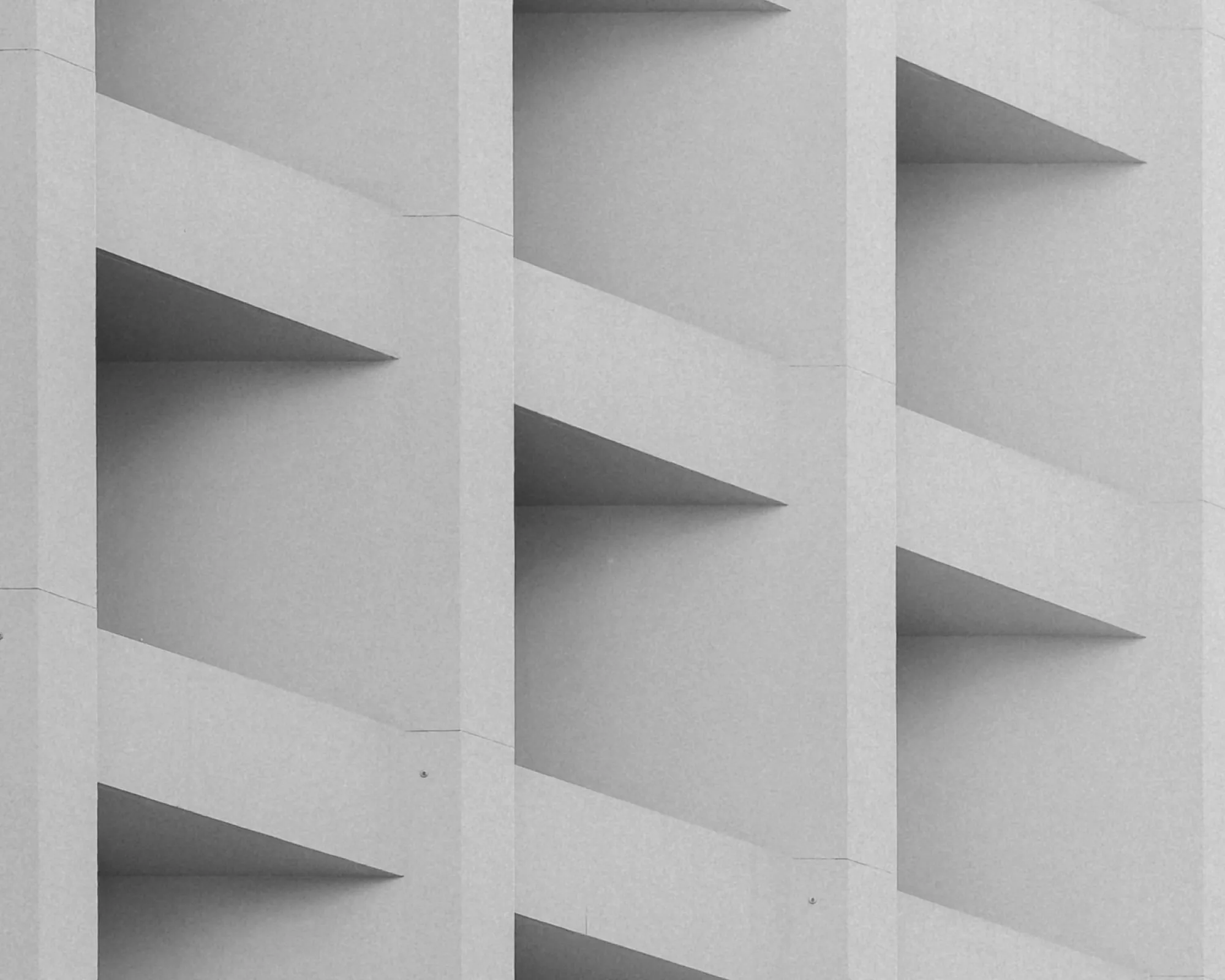 Close-up view of a gray concrete building facade showing diagonal shadows cast on vertical and horizontal structural elements.