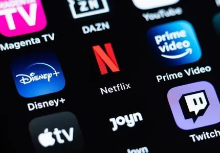 Close-up of a smartphone screen showing icons of popular streaming services including Disney+, Netflix, Prime Video, Apple TV, Magenta TV, DAZN, Joyn, YouTube, and Twitch.