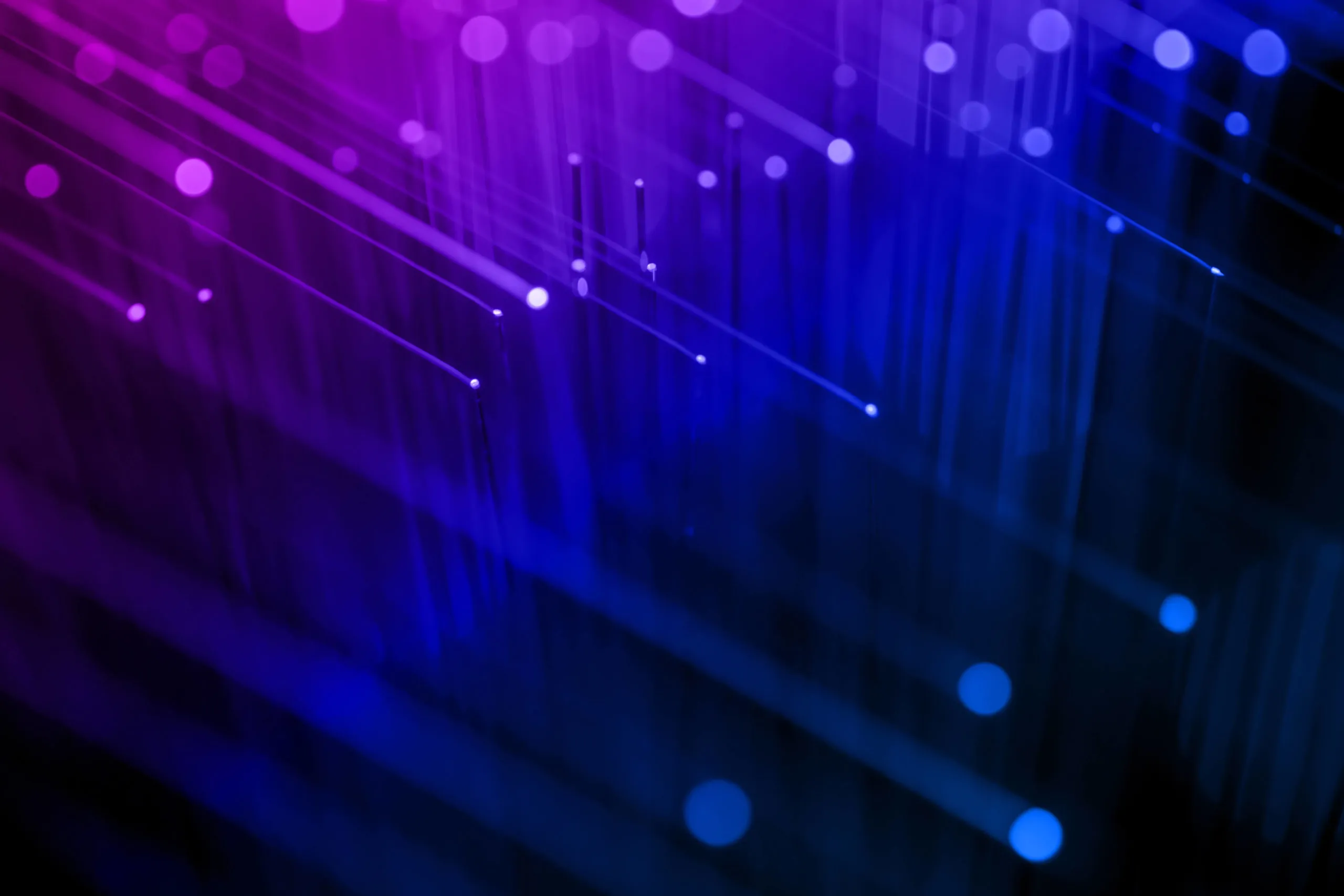Close-up view of fiber optic cables emitting glowing purple and blue light beams against a dark background.
