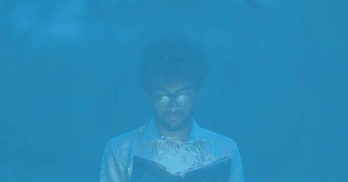 Man with curly hair and glasses reading a book that emits glowing light and magical energy.