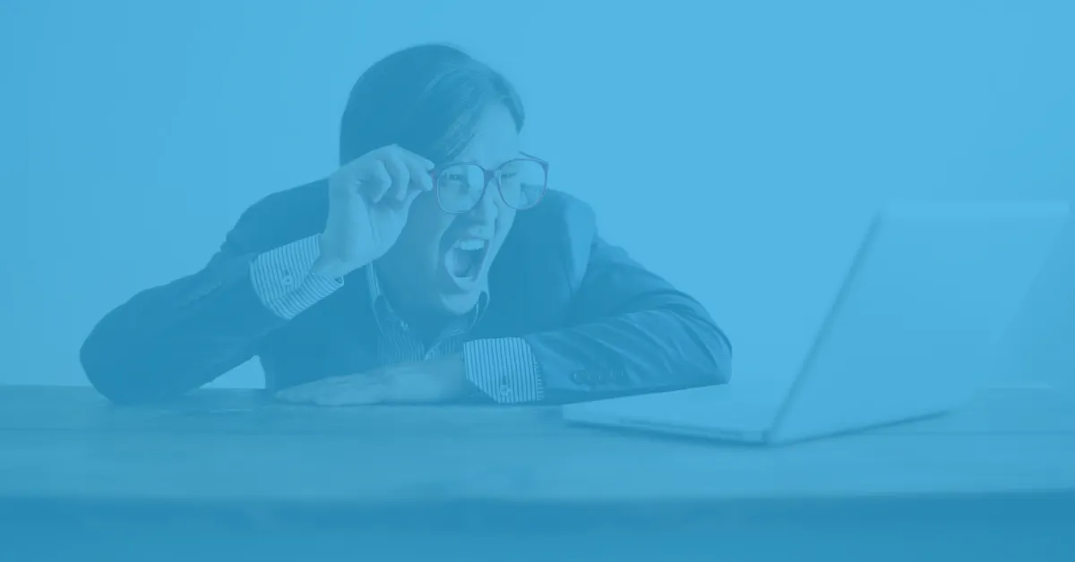 Person in business attire leaning on a table with a laptop, holding their glasses and yelling at the screen.