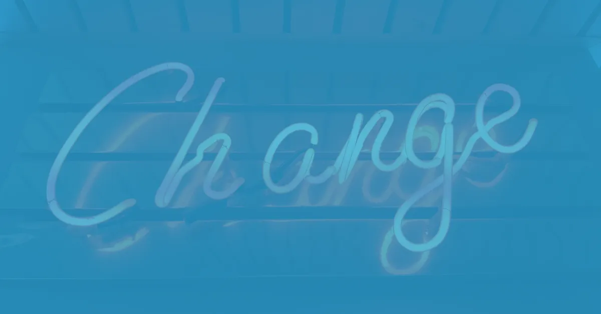 White neon sign spelling the word 'Change' in cursive letters mounted on a dark wall with horizontal beams visible behind.