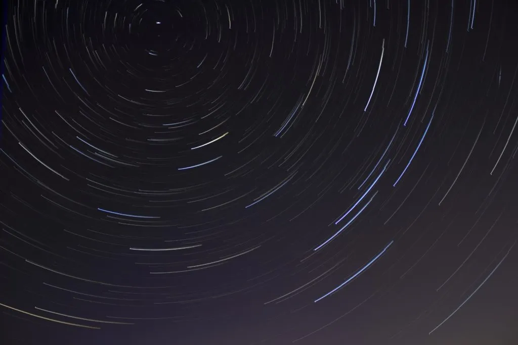 Long-exposure photograph of star trails forming circular patterns in the night sky against a dark background.