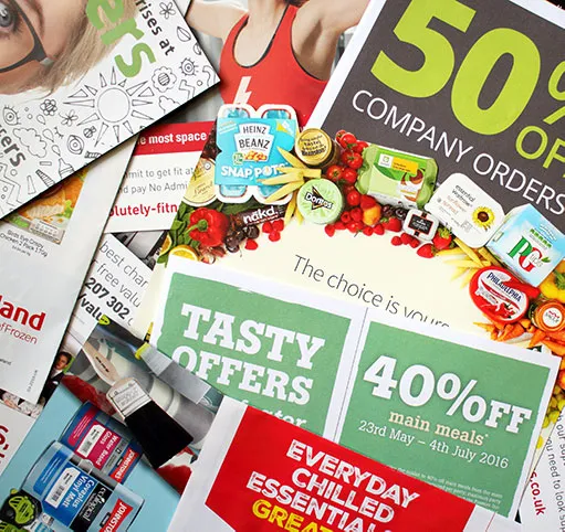 Overhead view of various colorful promotional flyers and leaflets featuring food discounts and offers, such as 50% off company orders, 40% off main meals from 23rd May to 4th July 2016, and everyday chilled essentials deals. Some flyers show images of fresh produce and packaged food products.