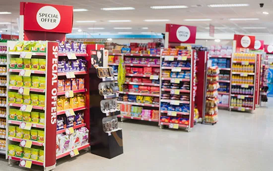 Supermarket aisle with multiple shelves stocked with various products and signs reading Special Offer on red display boards.