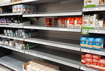 Supermarket shelf mostly empty, with some remaining packaged food items including rice and other products on top and sides.