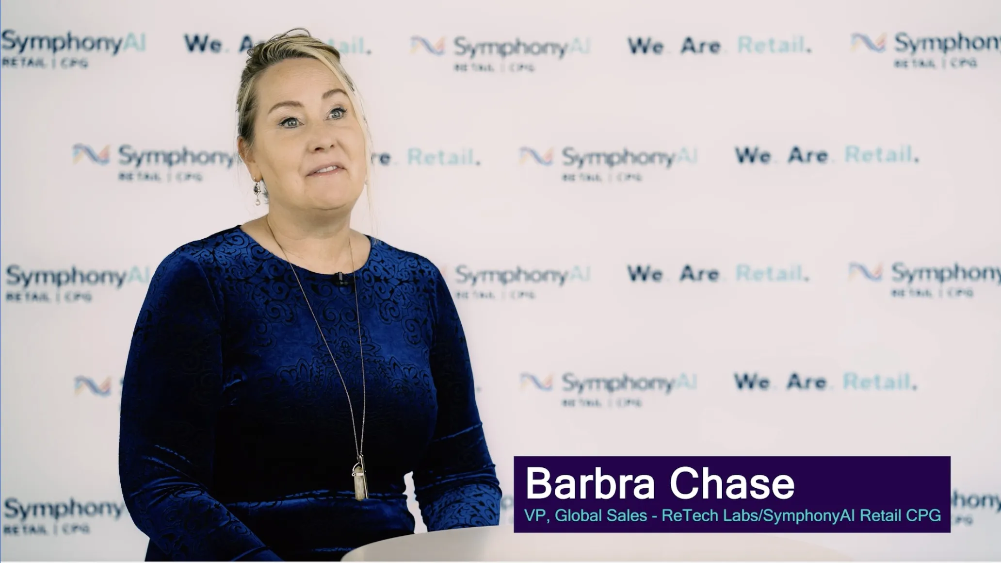 Barbra Chase, VP of Global Sales at ReTech Labs/SymphonyAI Retail CPG, sitting and speaking in front of a backdrop with the SymphonyAI and We Are Retail logos.