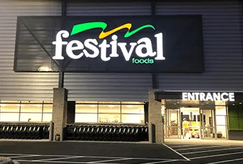 Festival Foods store entrance at night with illuminated store sign and parking lot in front.
