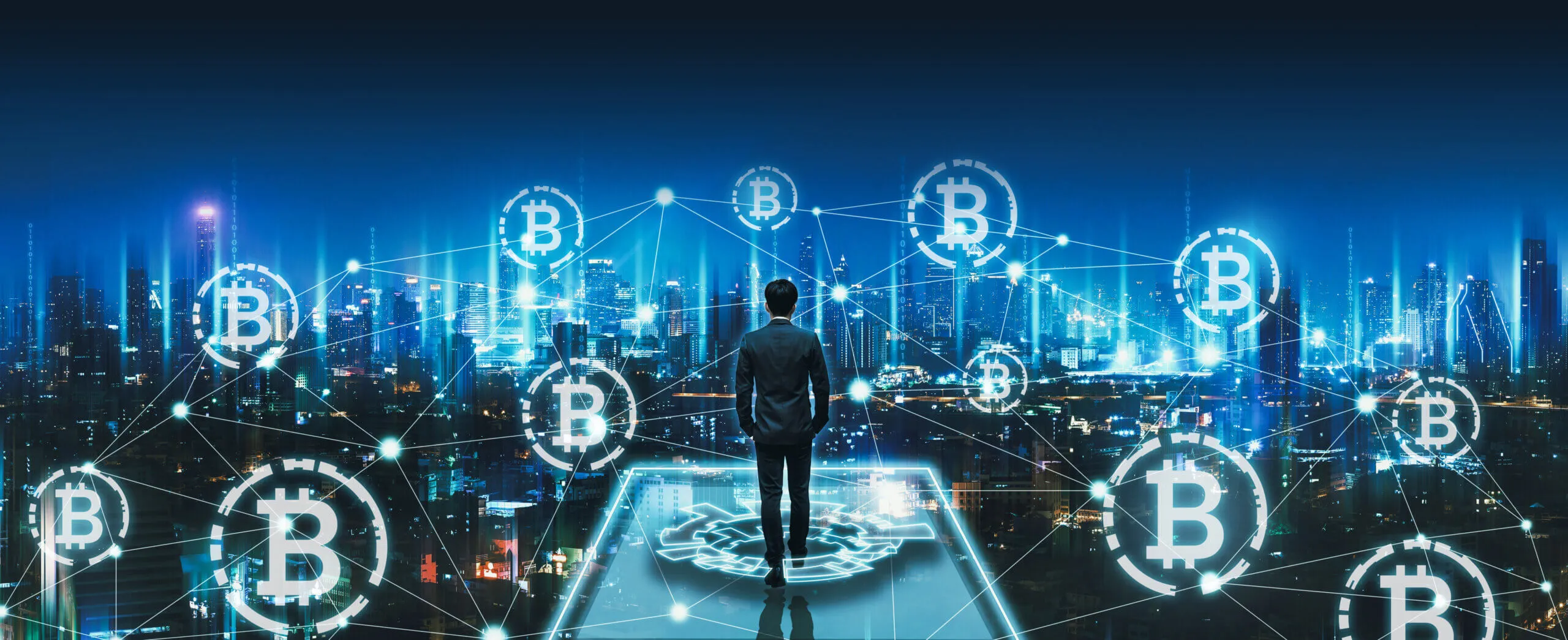 Man in business suit standing and looking over a city skyline at night with glowing interconnected Bitcoin symbols floating in the air, representing cryptocurrency and blockchain network.