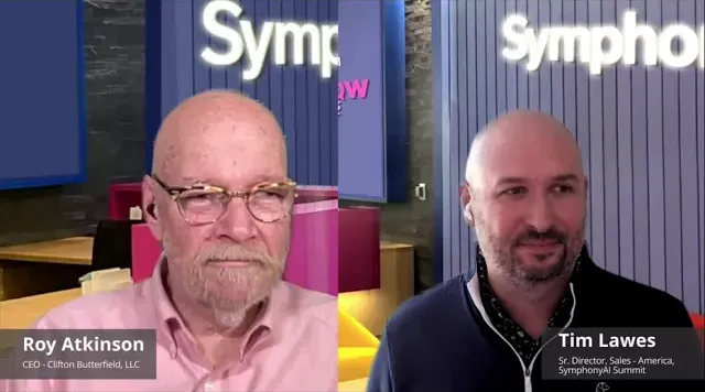 Split-screen video call of two men in front of SymphonyAI backgrounds. On the left is Roy Atkinson, CEO of Clifton Butterfield, LLC, wearing glasses and a pink shirt. On the right is Tim Lawes, Sr. Director of Sales - America at SymphonyAI Summit, wearing a dark zip-up jacket and earbuds.