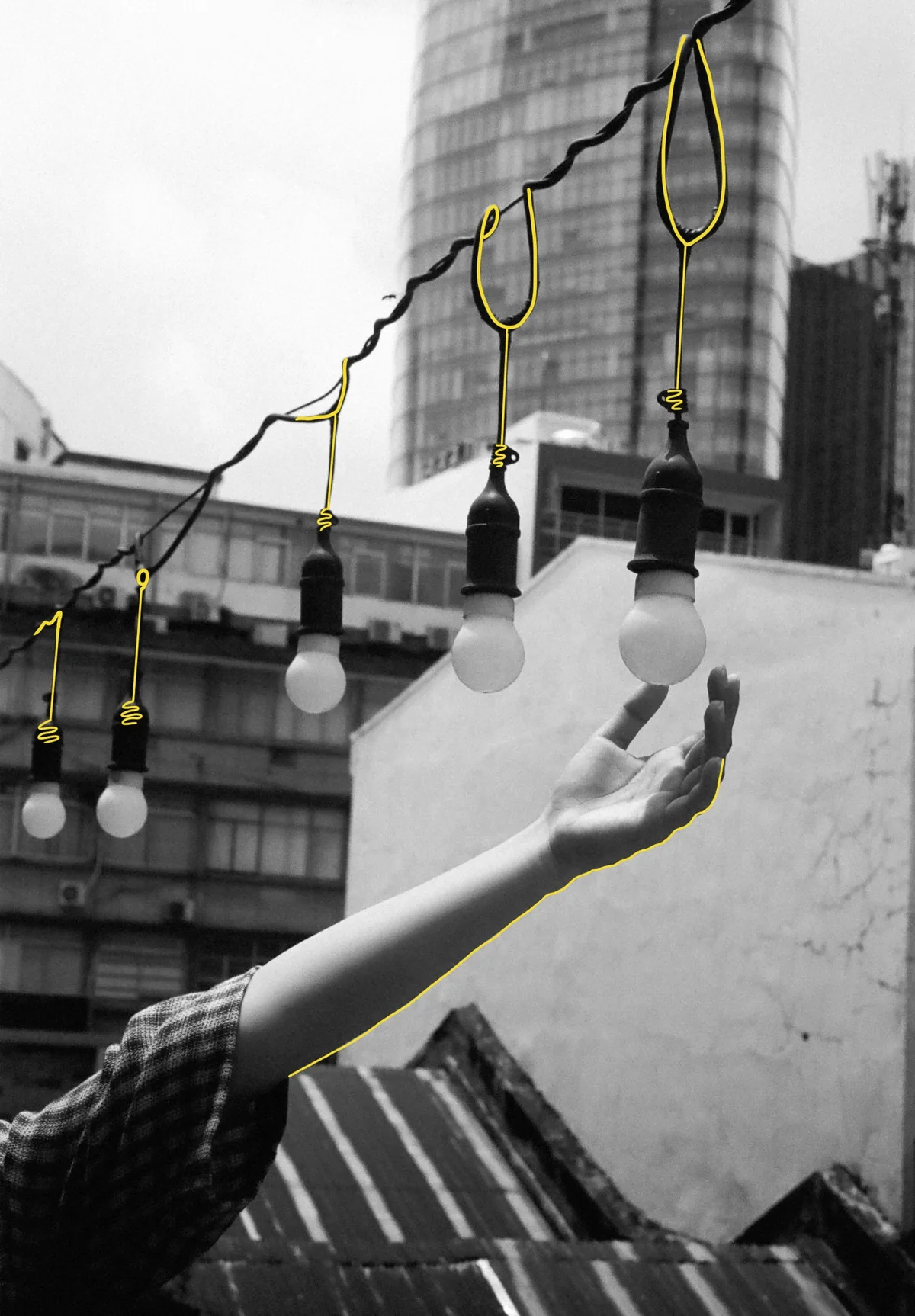 Hand reaching for hanging lightbulbs illuminated against a city building backdrop