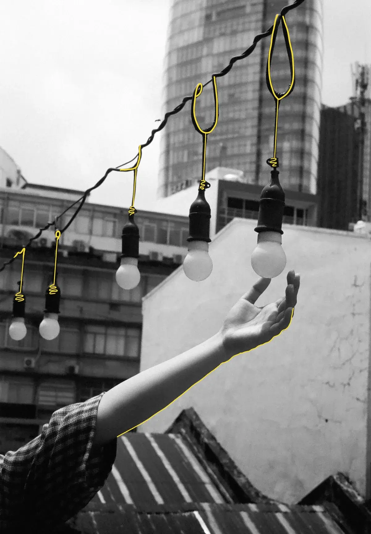 Hand reaching for hanging lightbulbs illuminated against a city building backdrop