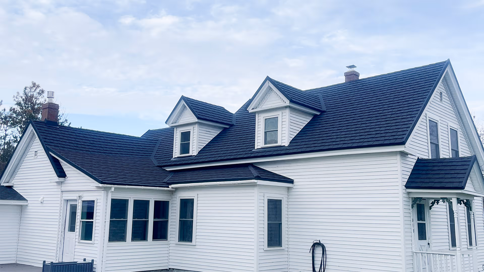 White wooden house with a dark gray shingle roof featuring two dormer windows and chimneys.