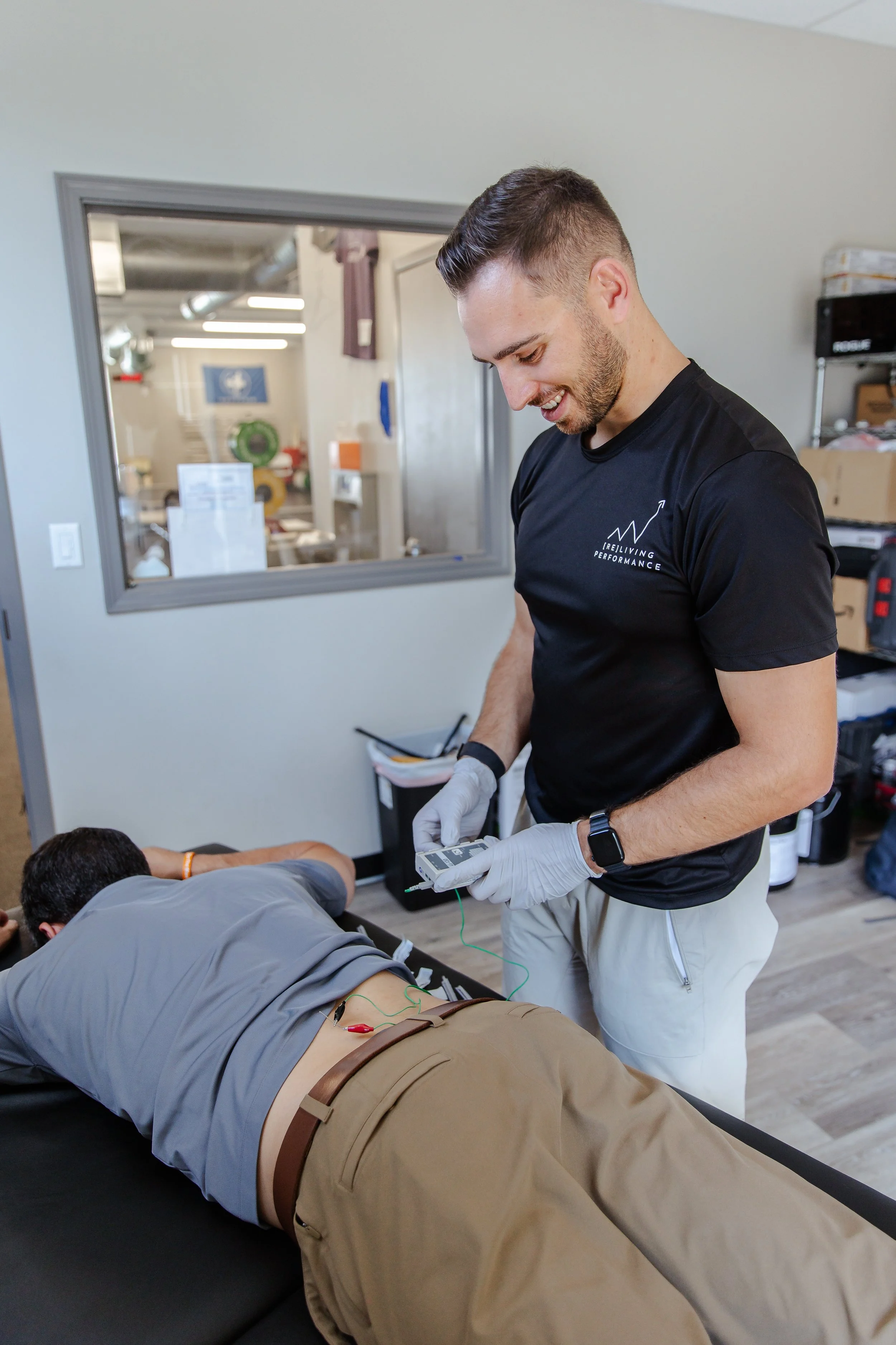 Therapist wearing gloves attaches electrodes to a patient’s lower back during treatment in a clinical room.