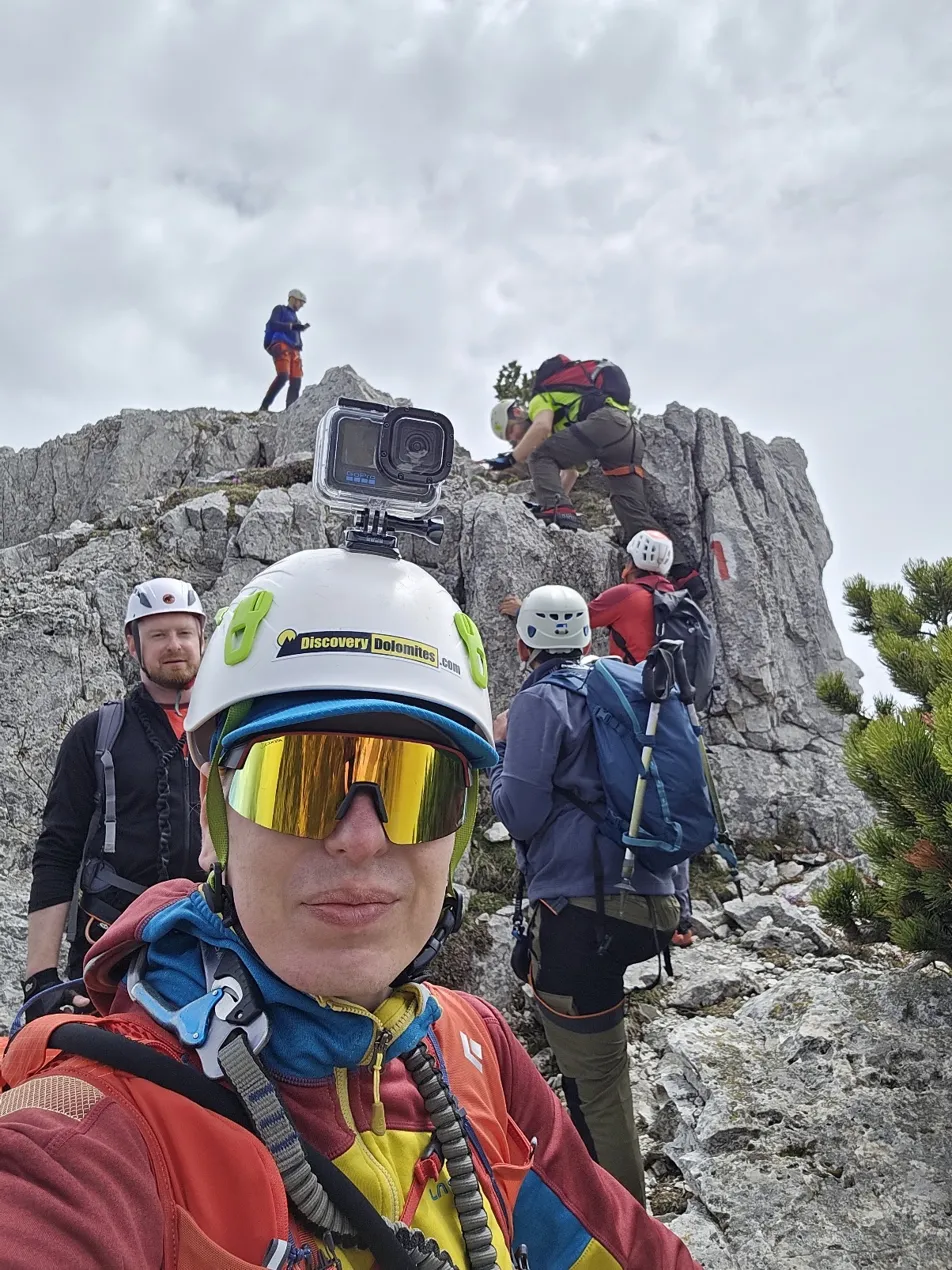 GoPro selfie on a rocky ridge — guide filming the group ascending behind him during a Geeks Go Peaks scramble