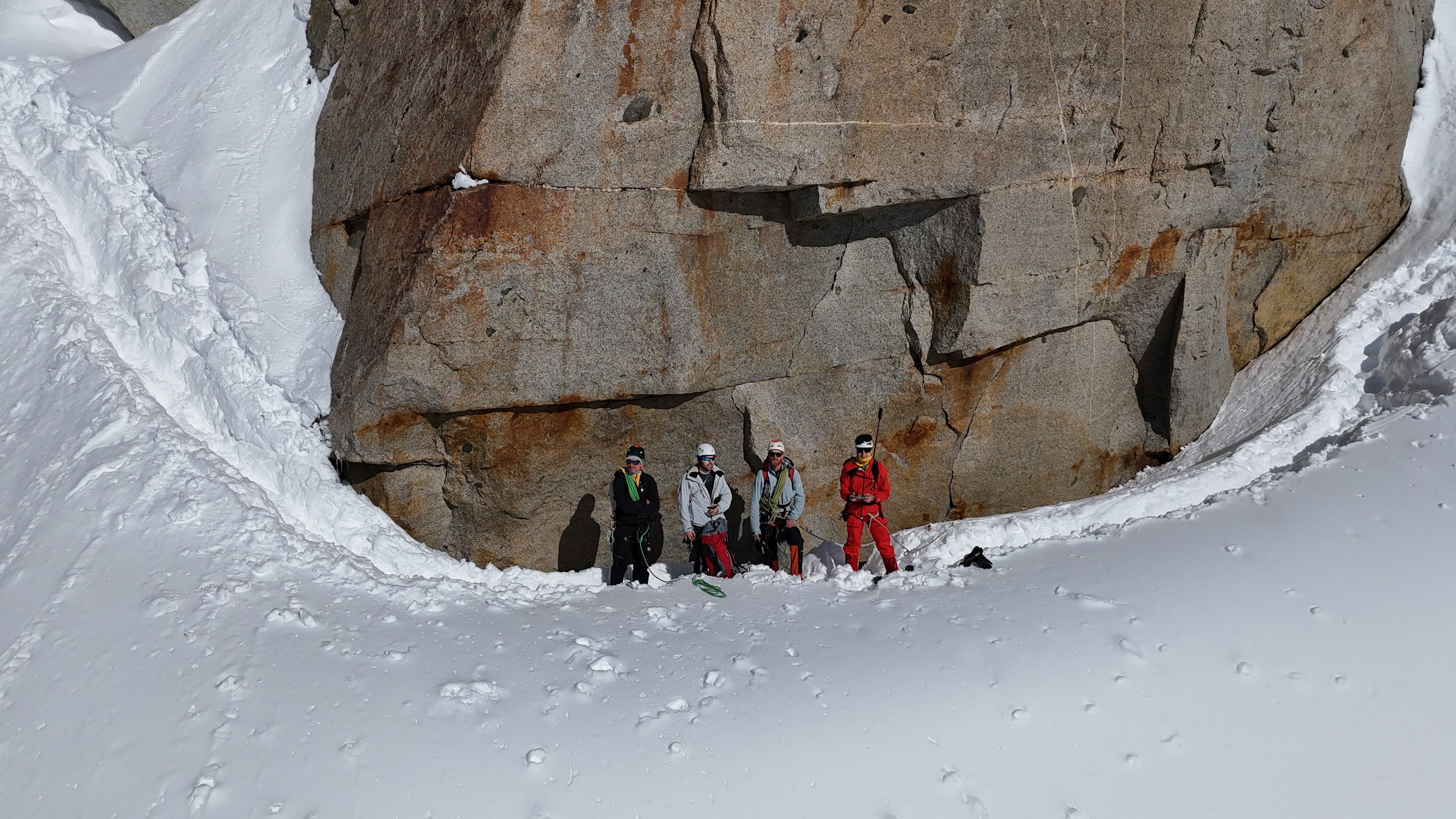 The team sheltering at the base of a large granite boulder on the Arête des Cosmiques, surrounded by deep snow