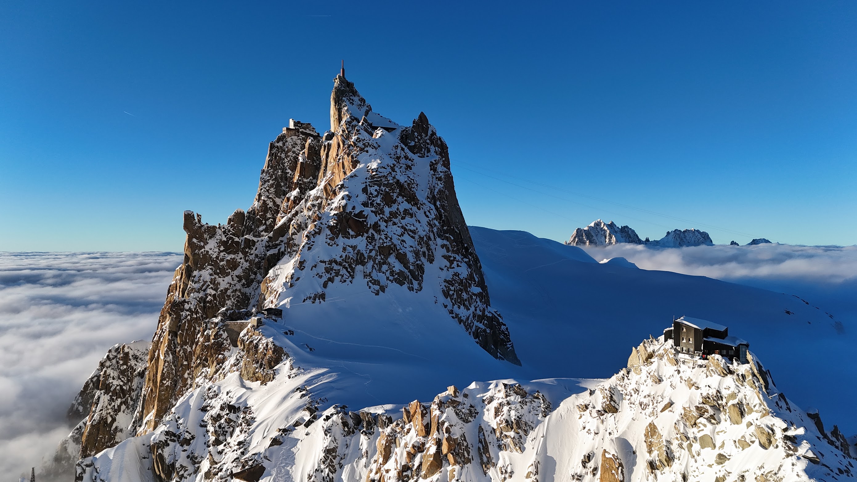 Aiguille du Midi spire and Refuge des Cosmiques rising above a sea of clouds, deep blue sky, French Alps
