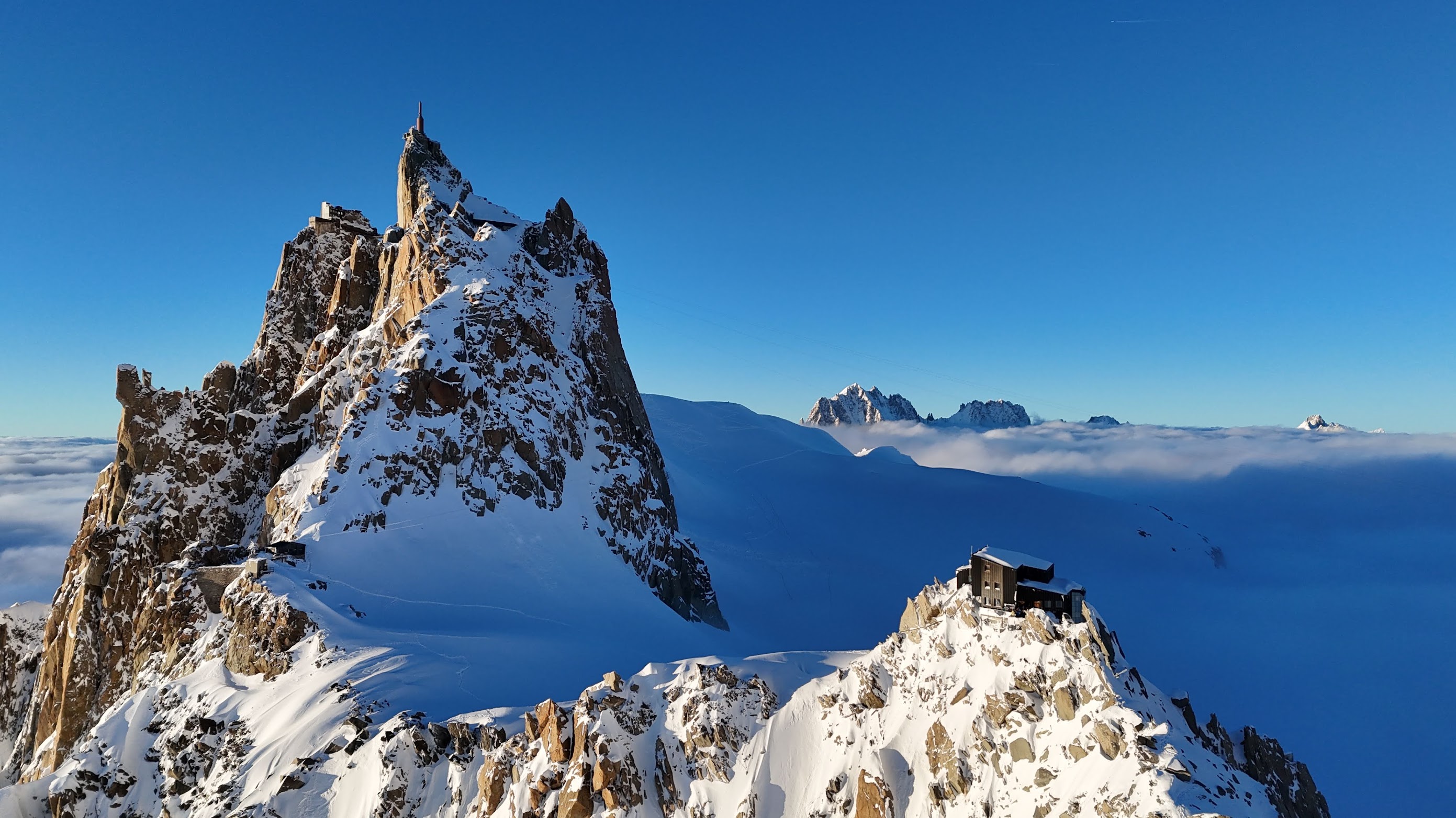 Aerial view of the jagged granite Aiguille du Midi massif surrounded by snow, peaks emerging from a sea of cloud
