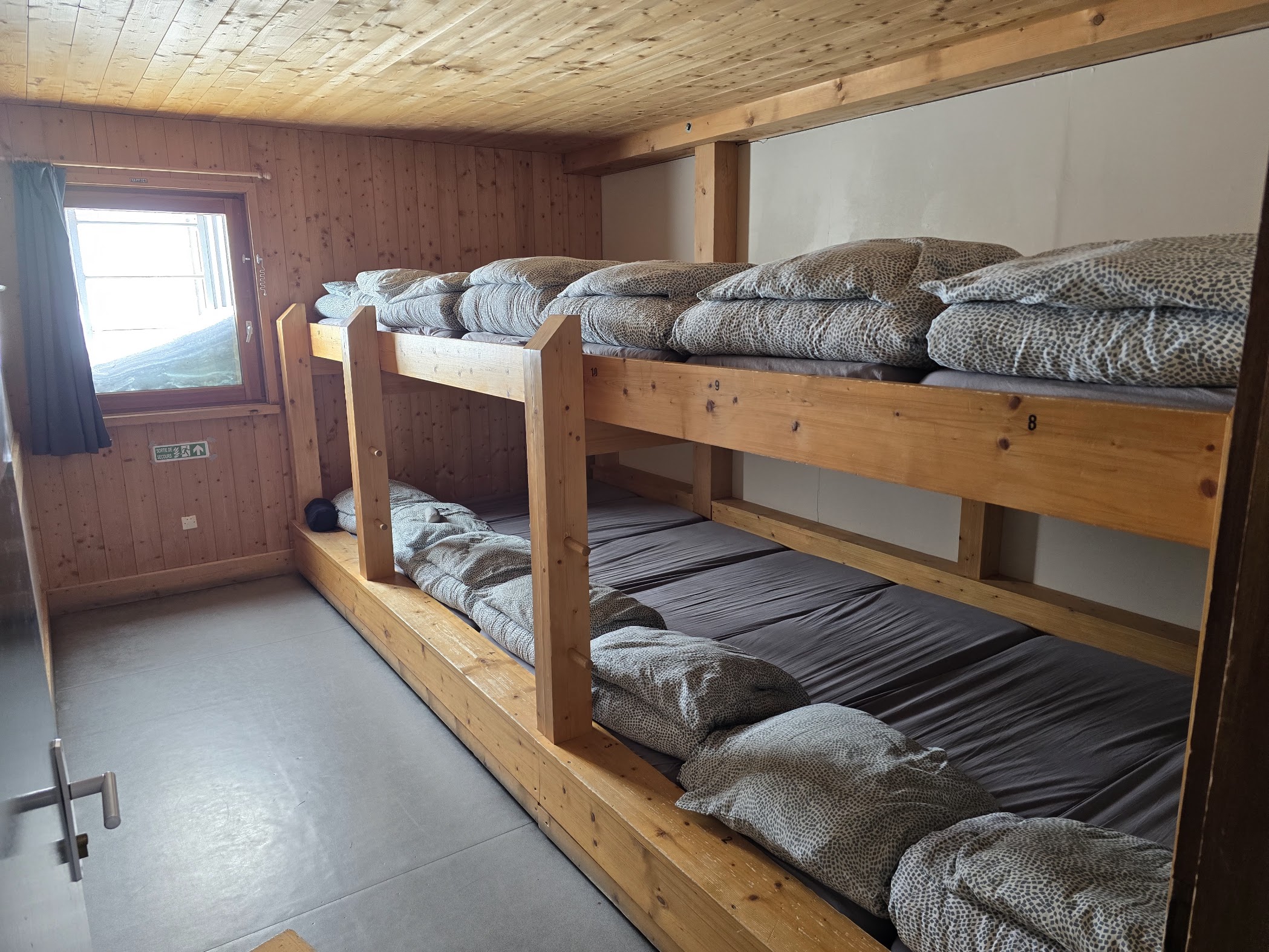 Wooden bunk beds with numbered mattresses inside the dormitory at Refuge des Cosmiques, 3,613m