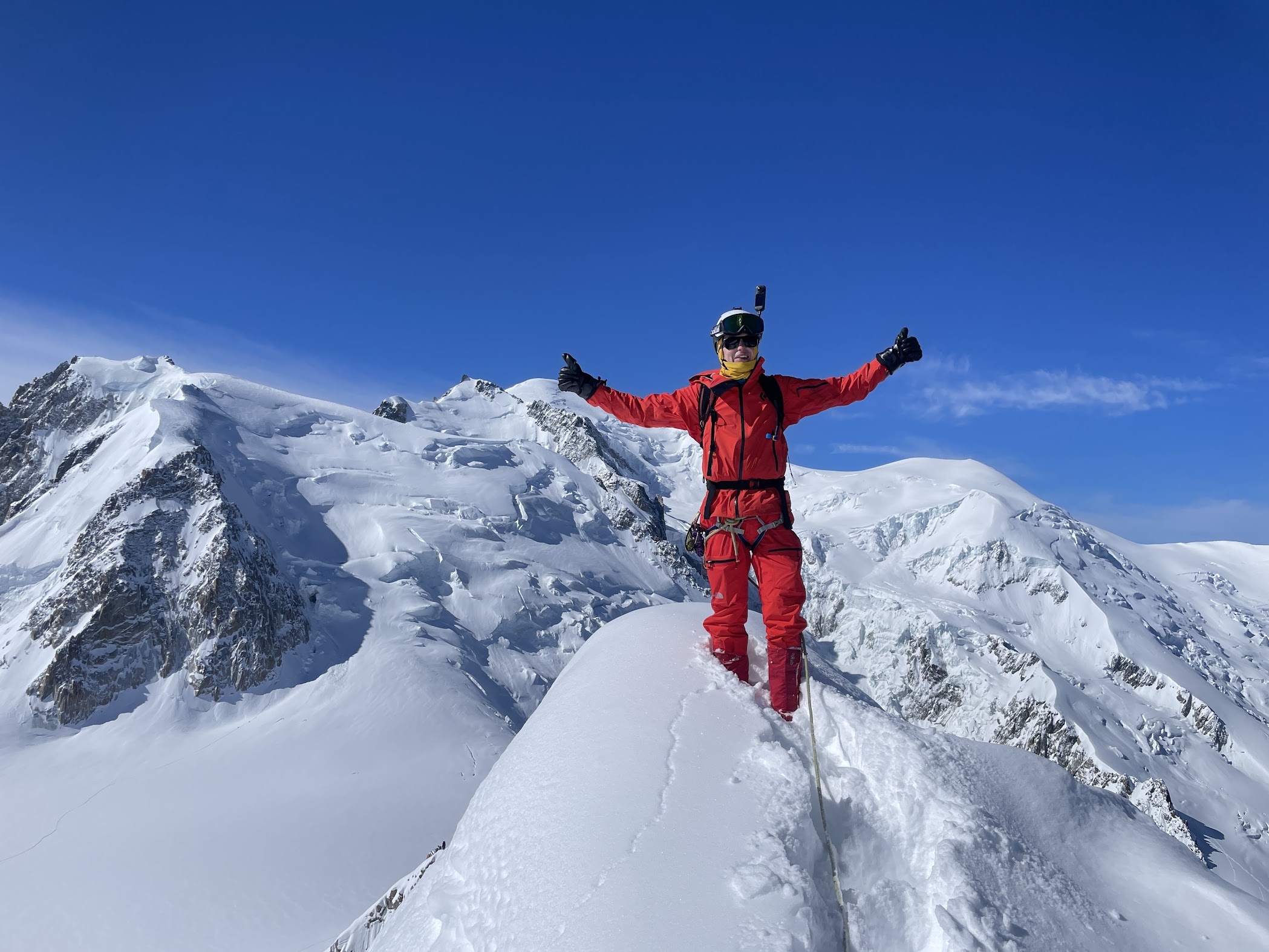 Peter Zaitsev on the Arête des Cosmiques ridge with arms wide open, Mont Blanc massif directly behind under a deep blue sky
