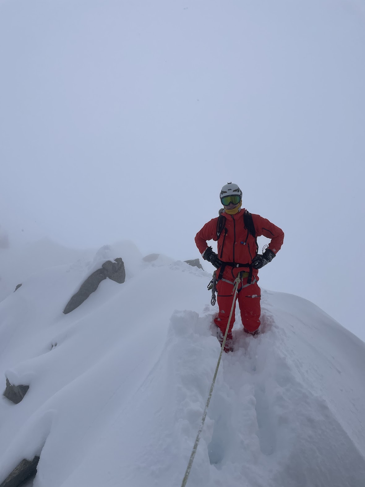 Climber in red suit navigating deep snow in complete whiteout on the approach to Refuge des Cosmiques