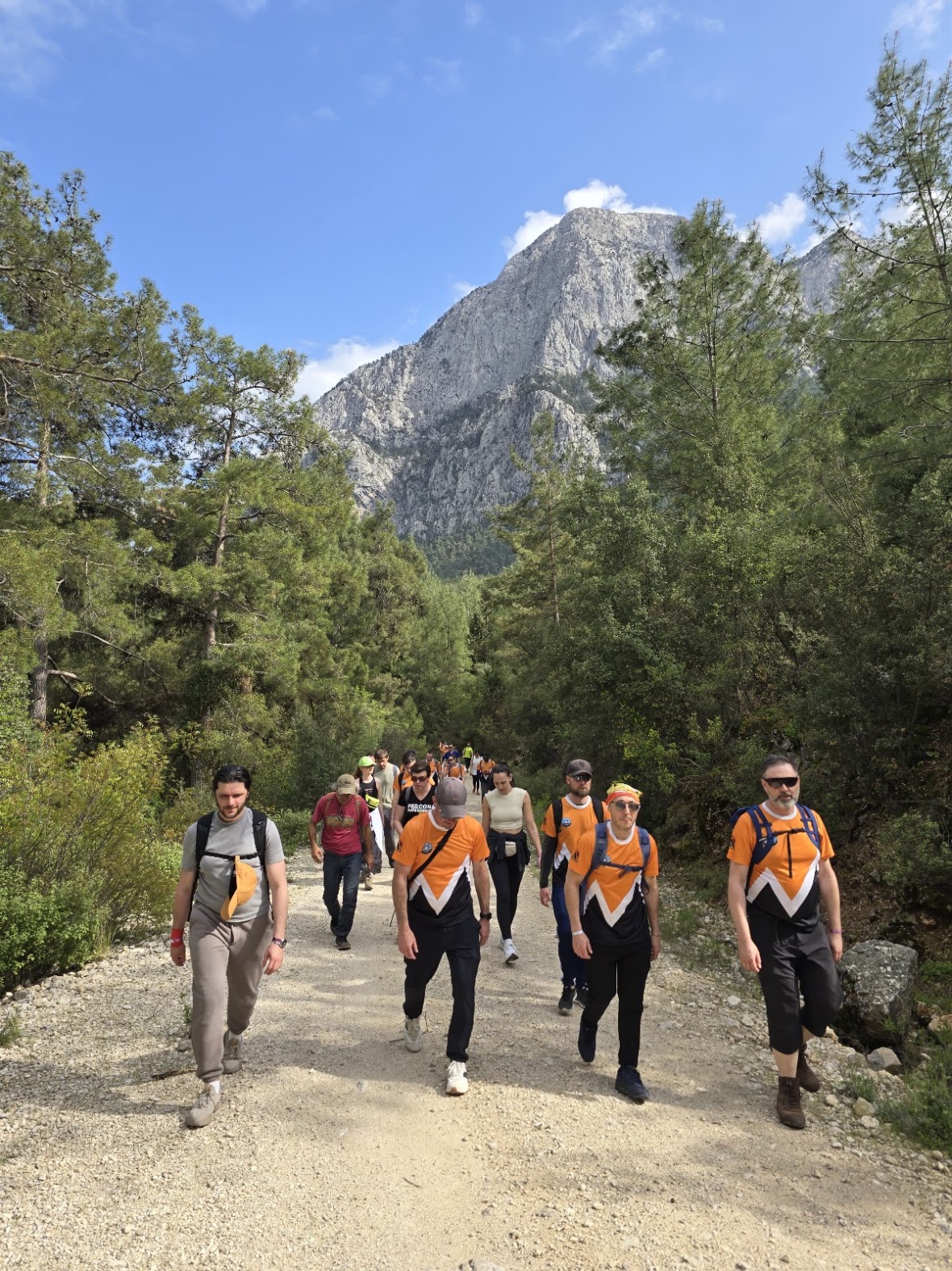 Percona team members in orange jerseys smiling together on the trail, mountains behind them