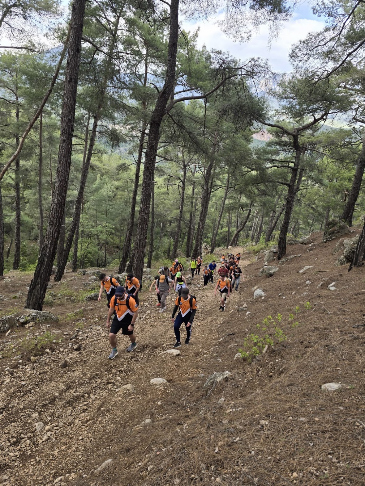 Percona team in orange jerseys hiking on a rocky trail above Geyikbayiri in the afternoon sun