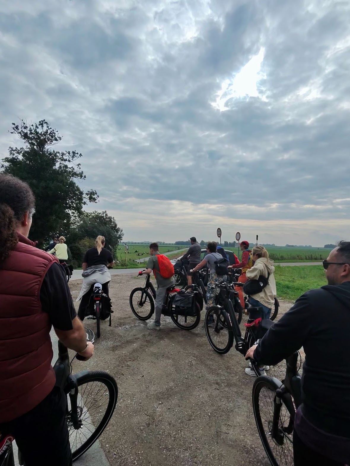 The group cycling e-bikes single file along a rural Waterland road under a cloudy sky