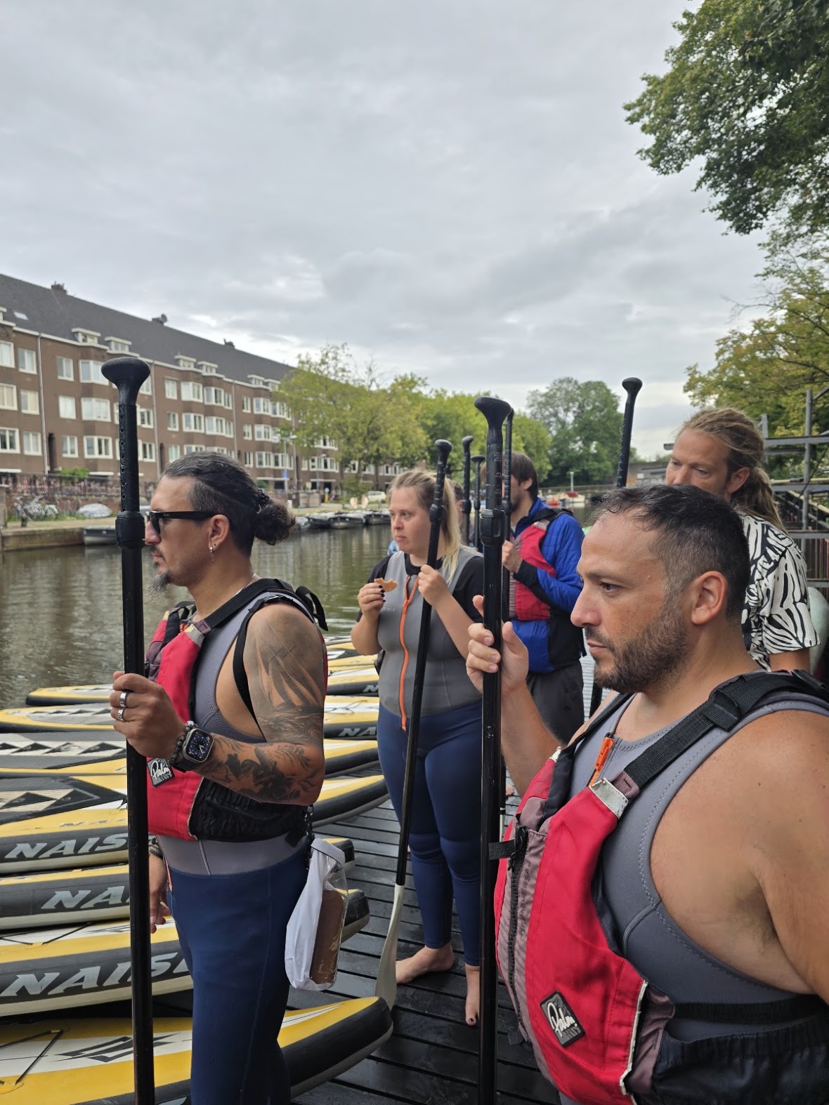 Participants in wetsuits and life vests holding paddles on a dock before setting out