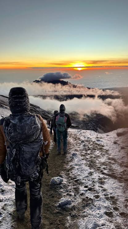 Climbers on a frosty trail near the summit as the sun rises above the clouds