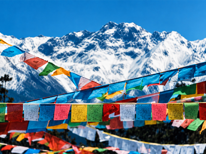 Rows of colourful Buddhist prayer flags in front of a snow-covered Himalayan range
