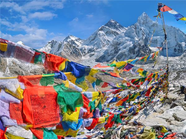 Colourful prayer flags strung over the rocks at Everest Base Camp with snowy Himalayan peaks behind