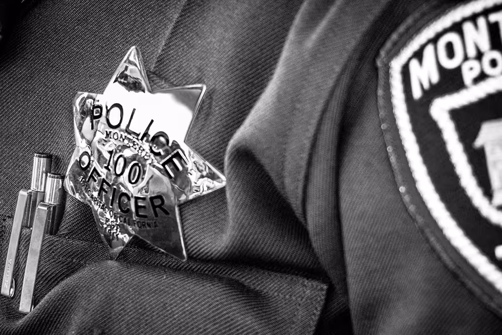 Close-up of a police officer's uniform displaying a shiny star-shaped badge and a fabric patch from Monterey Park Police Department.