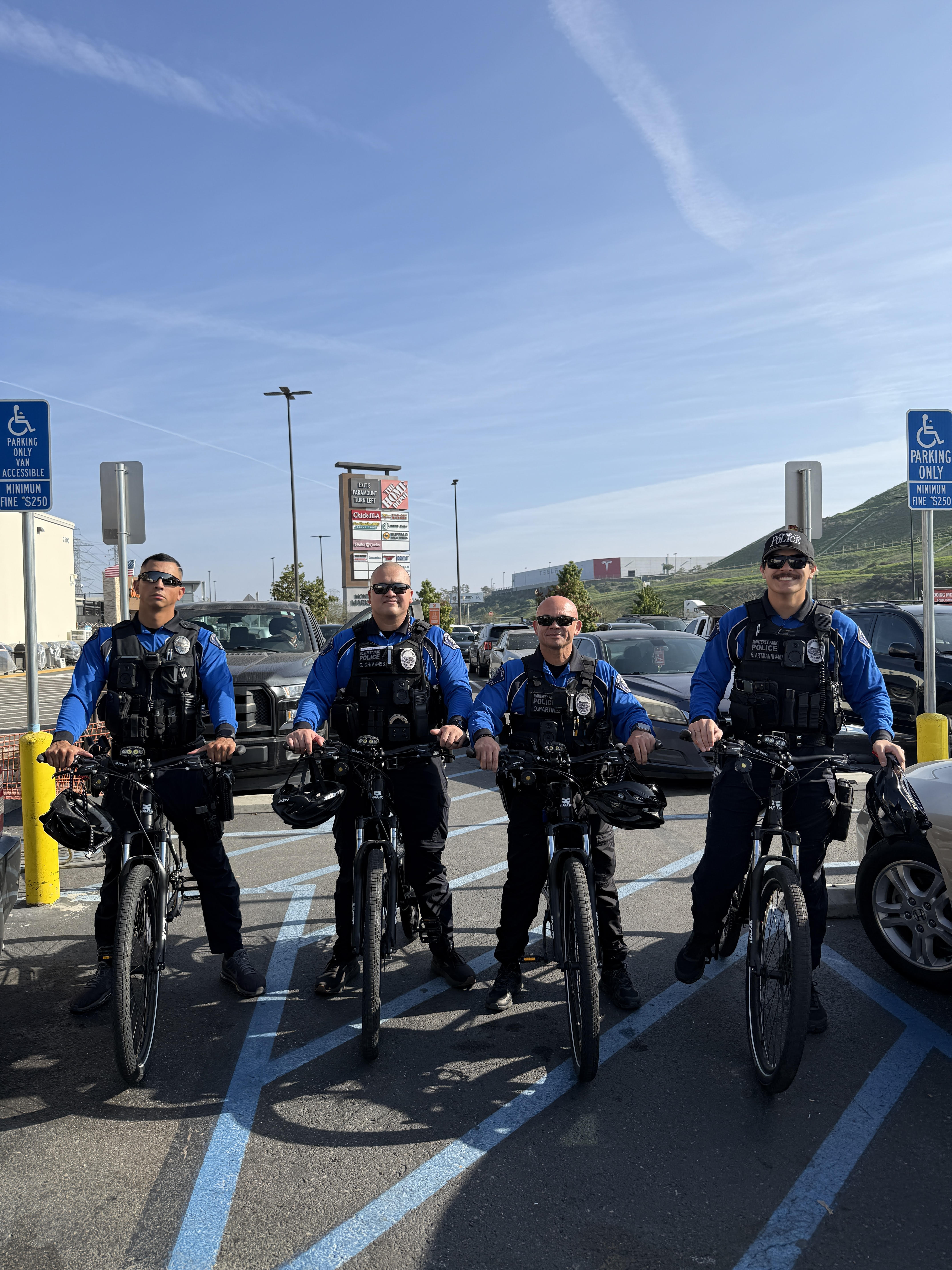 Four police officers in blue uniforms on bicycles in a handicapped parking area outdoors.