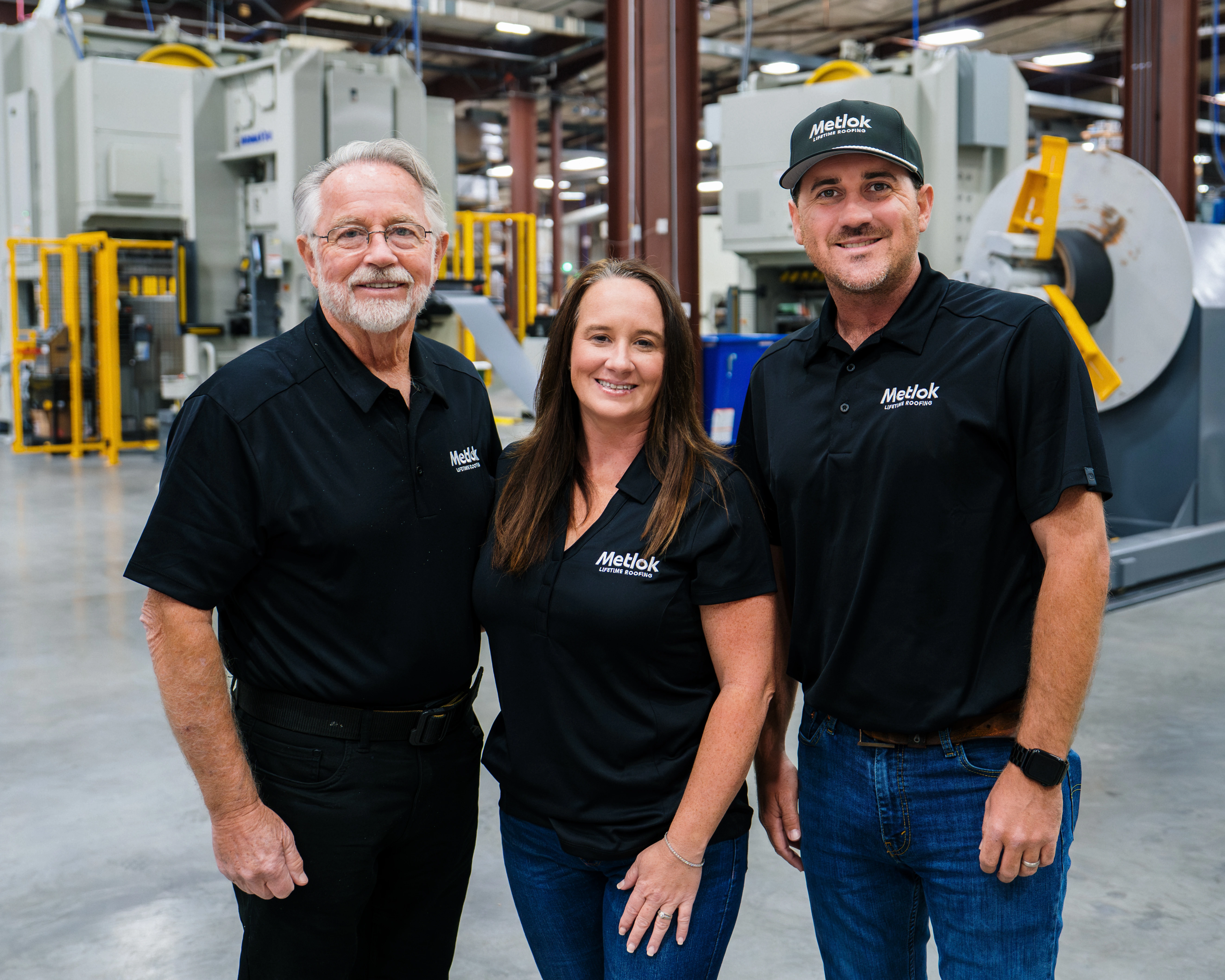 Three Metlok employees in black shirts and jeans standing in a manufacturing facility.