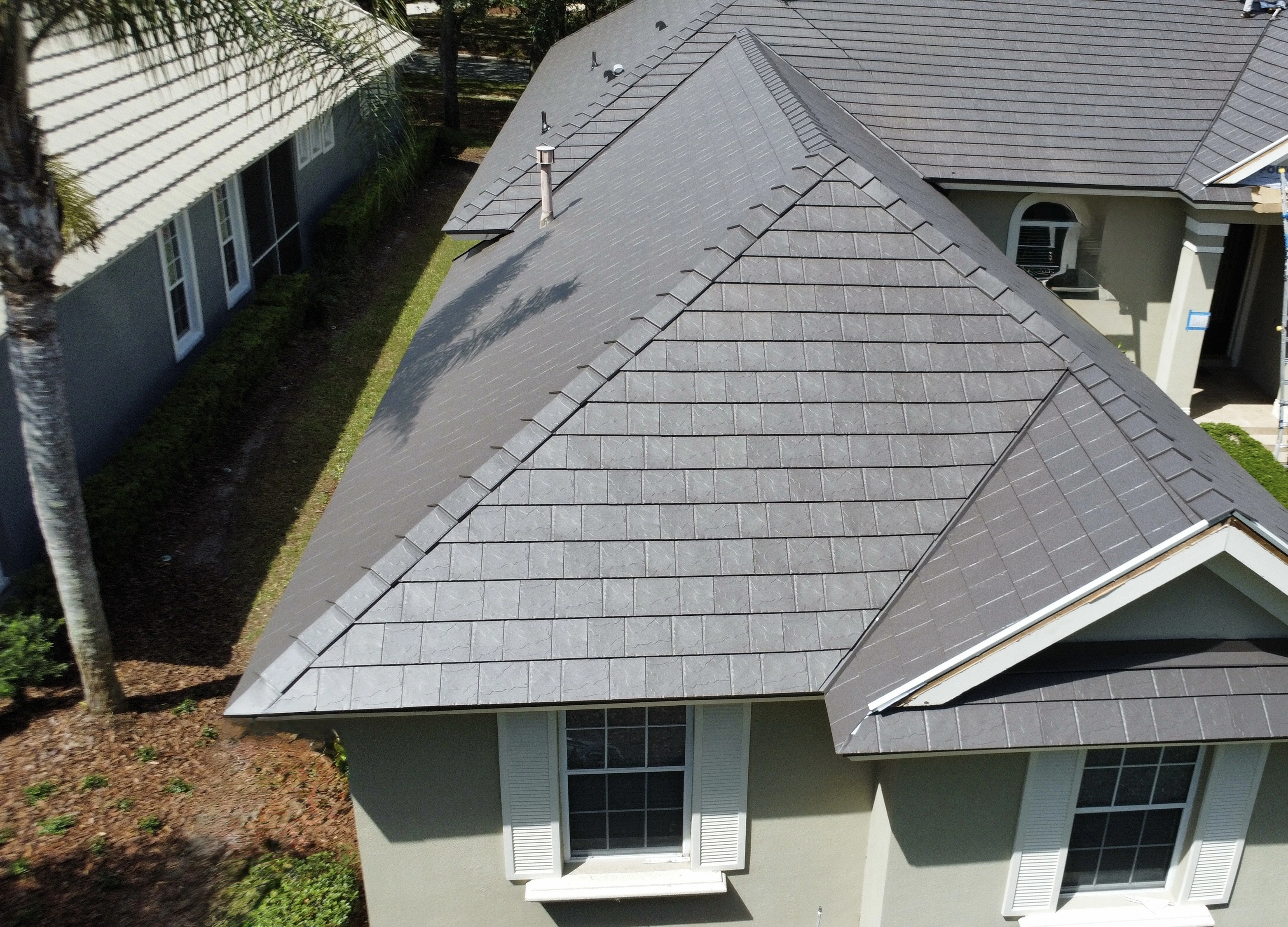 Aerial view of a house roof with gray shingles and surrounding landscaping.