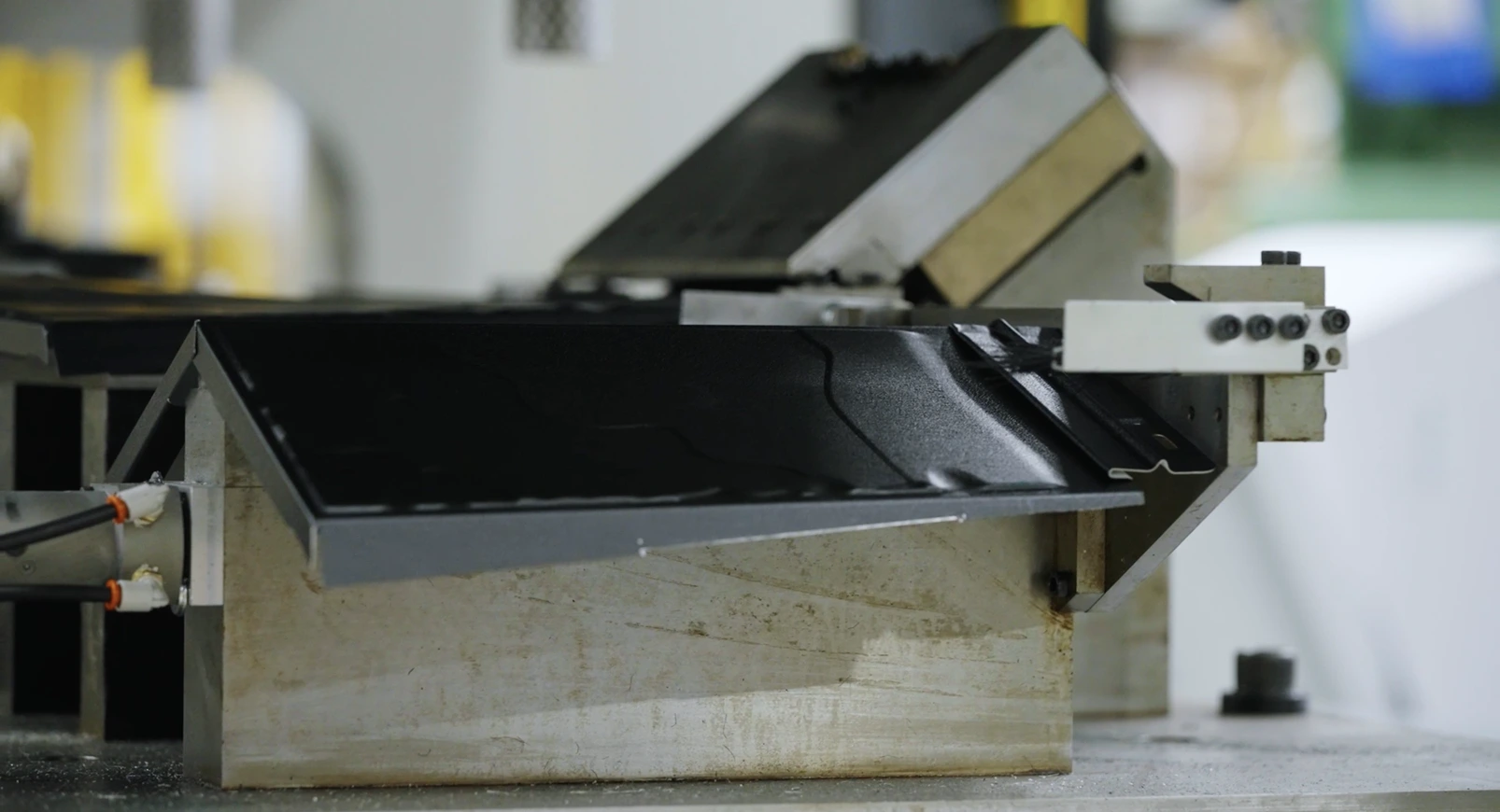 Close-up of a black metal sheet being shaped by an industrial machine.