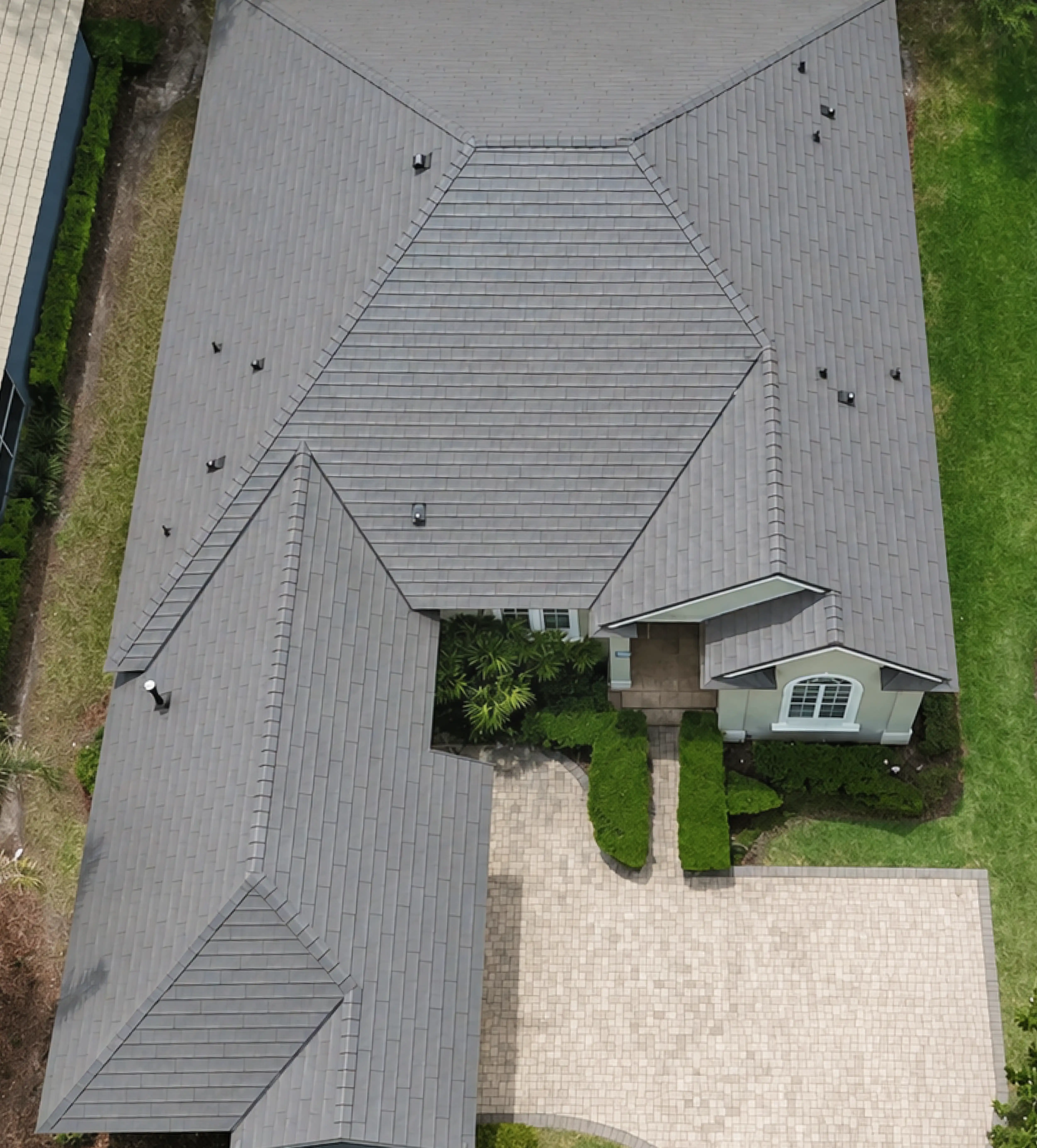 Aerial view of a gray tiled roof house with a paved driveway, green lawn, and shrubbery.