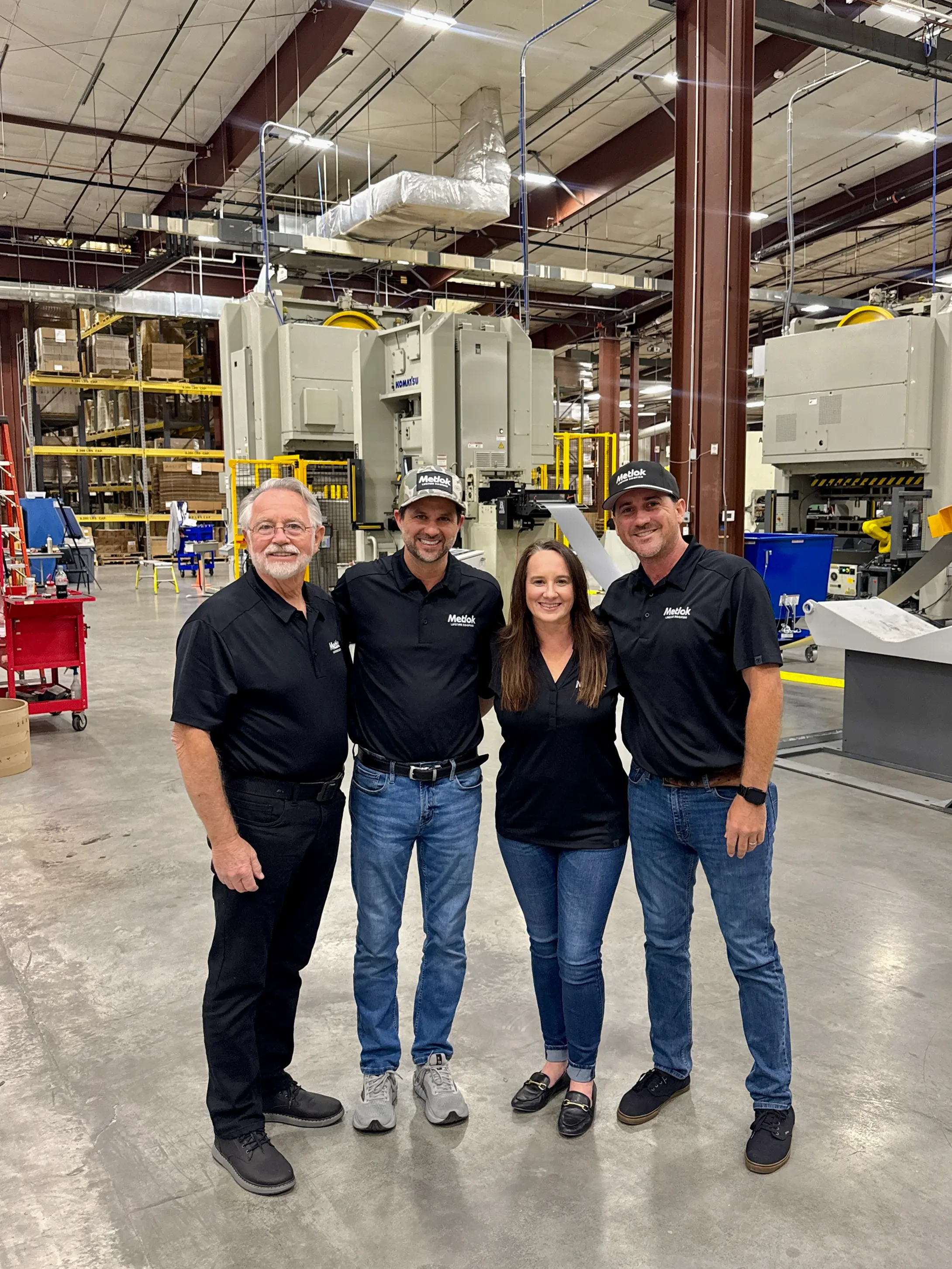 Group of four people in matching black Metlok shirts and jeans standing together in an industrial warehouse.