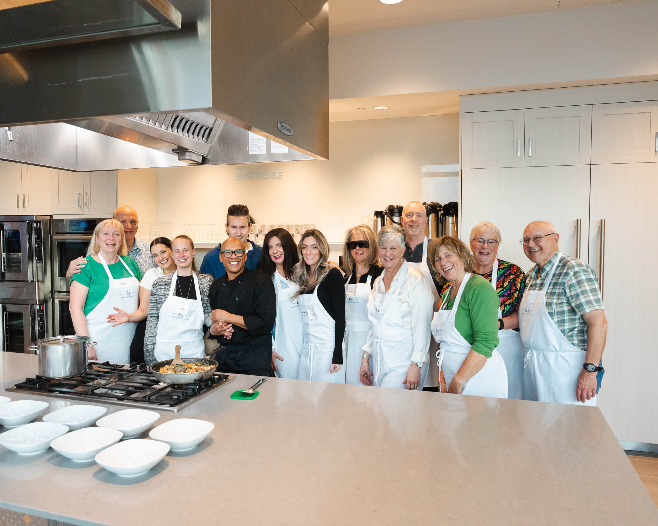 Chef Joey and participants in white aprons posing after a special event cooking class in Calgary