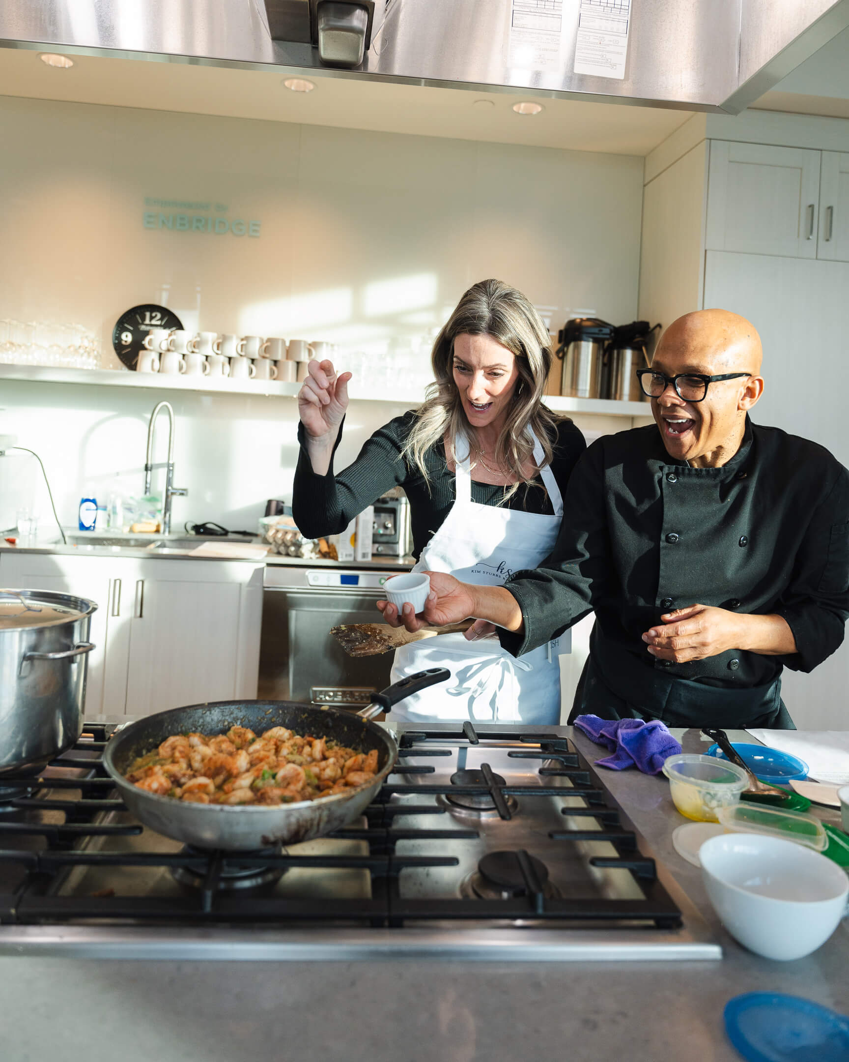 Chef Joey laughing with a student while cooking shrimp together during a hands-on cooking class