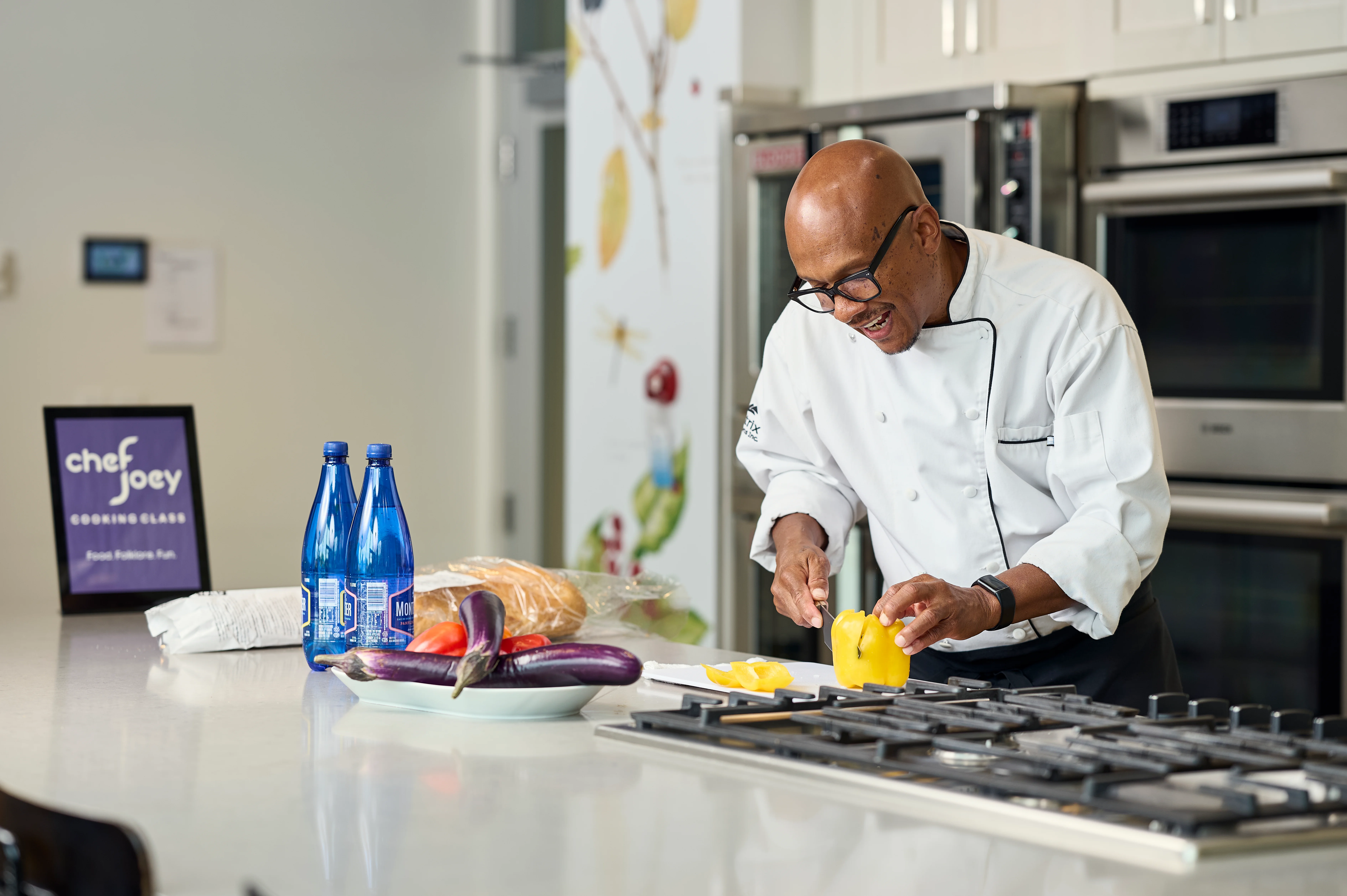 Chef Joey smiling while slicing yellow pepper at kitchen counter during a cooking class